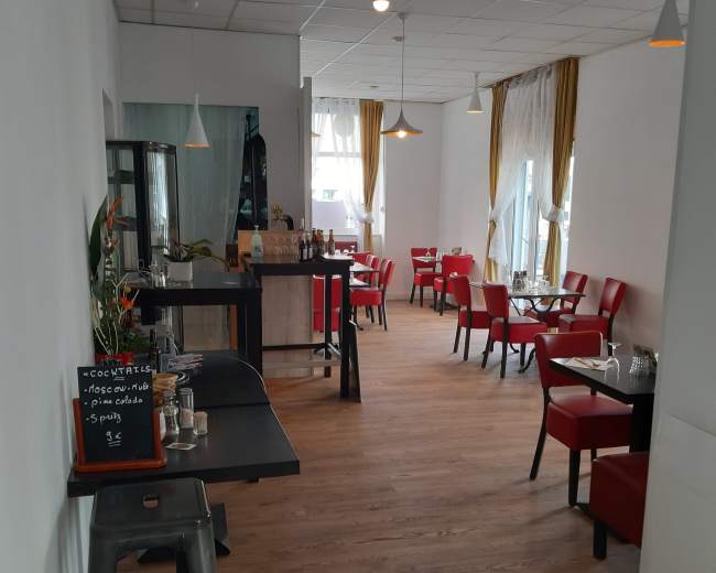 The image shows a spacious restaurant interior featuring red chairs, wooden flooring, and tables arranged along the walls.