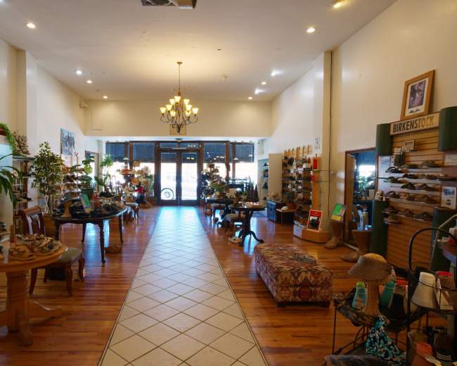 The image shows the interior of a shoe store featuring wooden flooring, displayed footwear on shelves, and a central seating area.
