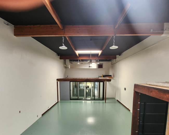 The image shows a spacious, empty interior room with a polished green floor and wooden beams overhead.
