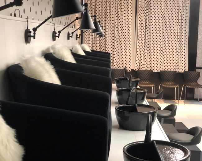 A modern salon interior with black chairs, wash basins, and decorative curtains featuring a polka dot pattern.