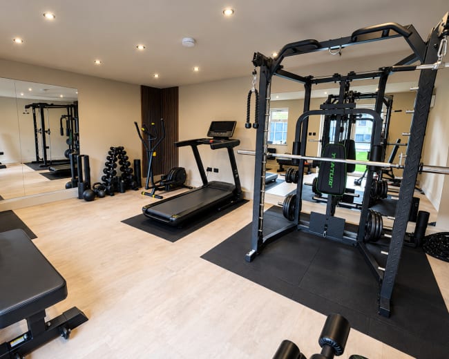 The image shows a spacious home gym equipped with a treadmill, weight bench, multi-station weight machine, and free weights.