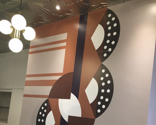 The image features a large wall mural with geometric shapes, including circles and lines, arranged in a stylized pattern of brown, black, and white.