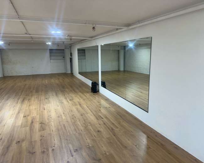 The image shows an empty dance studio with wooden flooring and large mirrors on the walls.
