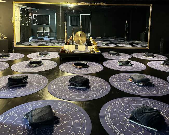 A dimly lit room with circular mats arranged on the floor, a large mirror at the back, and various sound instruments set up in the center.