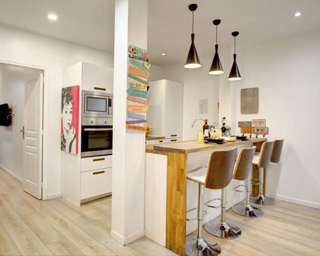 A modern kitchen features a wooden island with bar stools, white cabinetry, and pendant lighting.