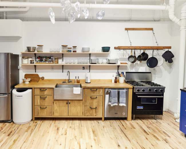 The kitchen features stainless steel appliances, a wooden countertop, open shelving with dishware, and hanging pots.