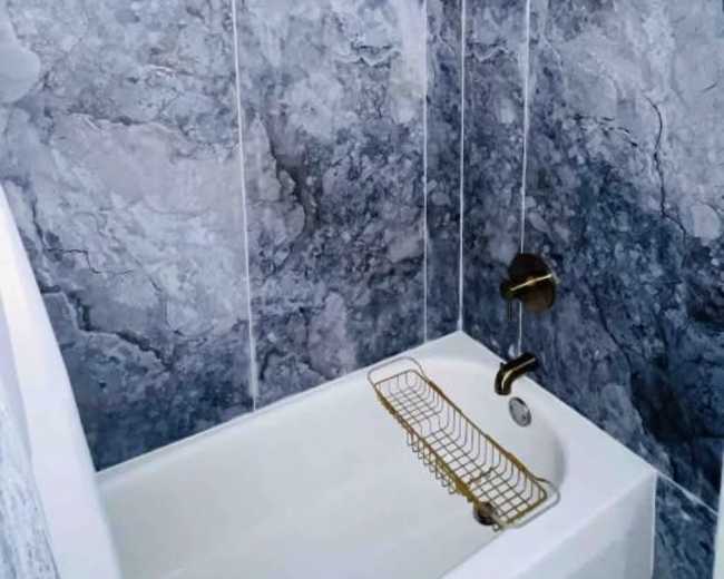 A compact shower area with blue-gray marbled tiles and a gold shower curtain rod.