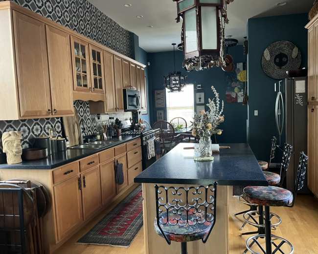 The kitchen features wooden cabinetry, a central island with bar stools, and patterned wall decor.