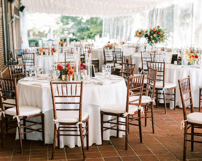 A beautifully arranged dining area with round tables covered in white tablecloths, set with floral centerpieces and surrounded by wooden chairs.
