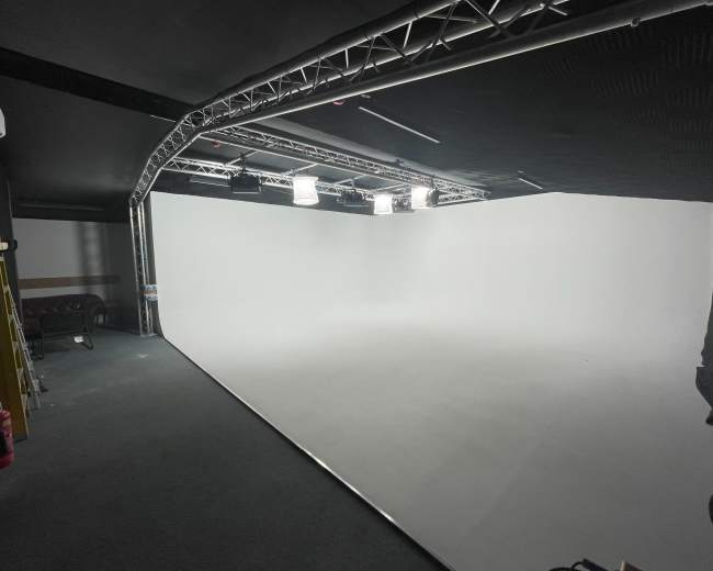 A minimalist studio space with a large white backdrop and overhead lighting.