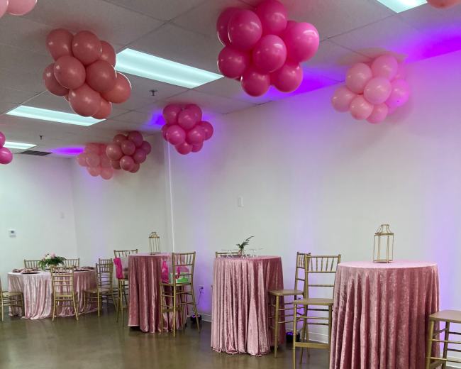 A room decorated with pink balloons and tables covered in pink tablecloths, set up for an event.