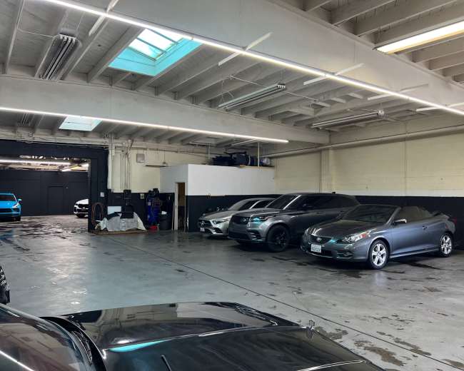 The image shows a spacious indoor parking area with several parked cars lined up along the walls.