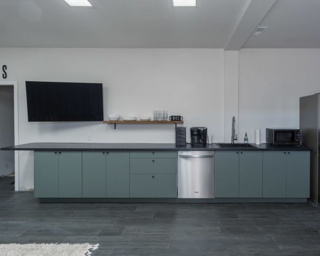 The image shows a modern kitchen with a long countertop, a refrigerator, a microwave, a coffee maker, and a wall-mounted television.