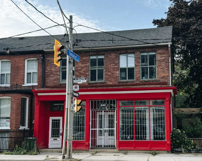 A brick building with a bright red storefront and large windows is situated at the corner of a street sign marked "Orleans."
