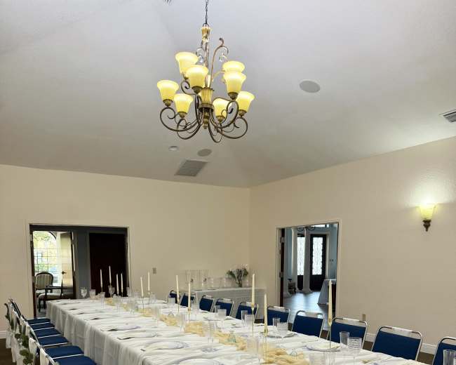 A long table is set for a formal dining event with white tablecloths and blue chairs, illuminated by a chandelier.
