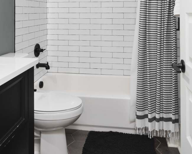 A modern bathroom featuring a white tiled shower with a black and white striped shower curtain, a black vanity, and a white toilet.