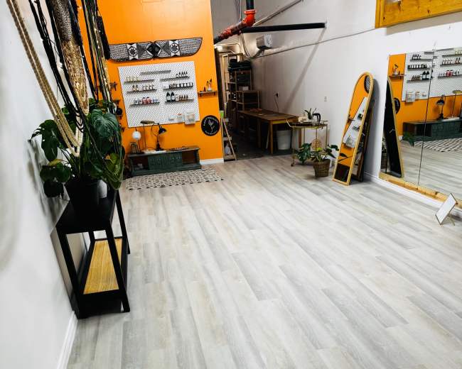 The image shows a spacious interior with light gray wooden flooring, a large mirror, and various items mounted on the wall.