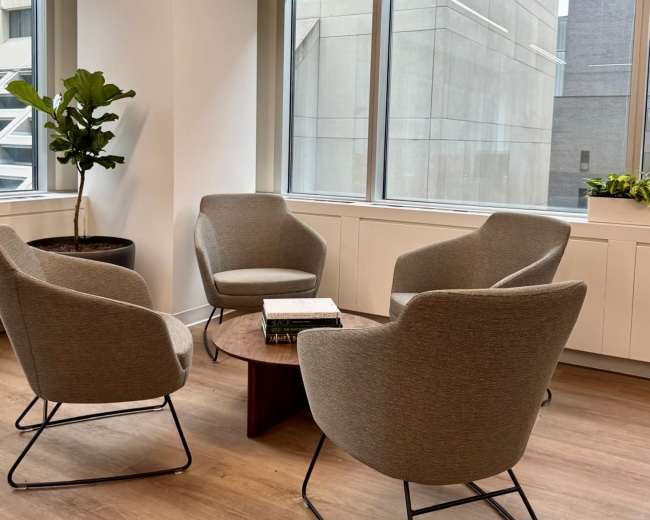 The image shows a modern office corner with four upholstered chairs arranged around a small table near large windows.
