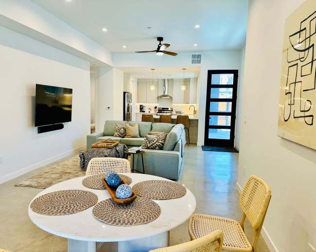 The image shows a modern, open-concept living space featuring a stylish seating area, a dining table, and a kitchen in the background.