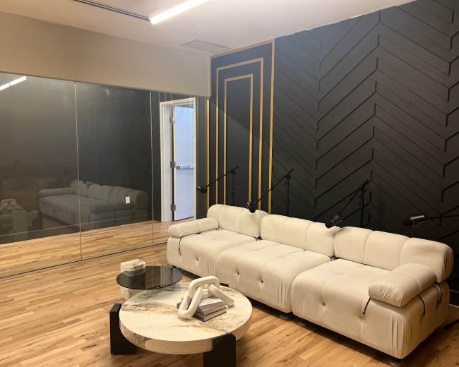 The image shows a modern lounge area featuring a beige sectional sofa, a marble coffee table, and a glass wall with a dark geometric-patterned accent wall behind it.