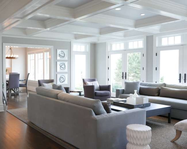 A spacious living room features a light gray sofa, a coffee table, and large windows that allow natural light to fill the space.