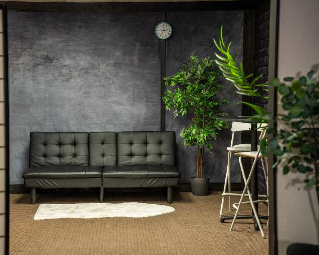 The image shows a modern interior space with a black leather sofa, a potted plant, and a wall clock against a textured backdrop.