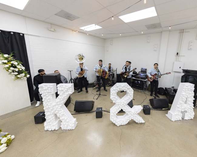A band performs on a small stage in front of large decorative letters spelling "K & A," surrounded by musical instruments and sound equipment.