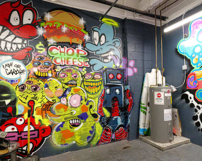 The image shows a corner of a room adorned with colorful graffiti featuring various cartoonish characters and designs on the walls.