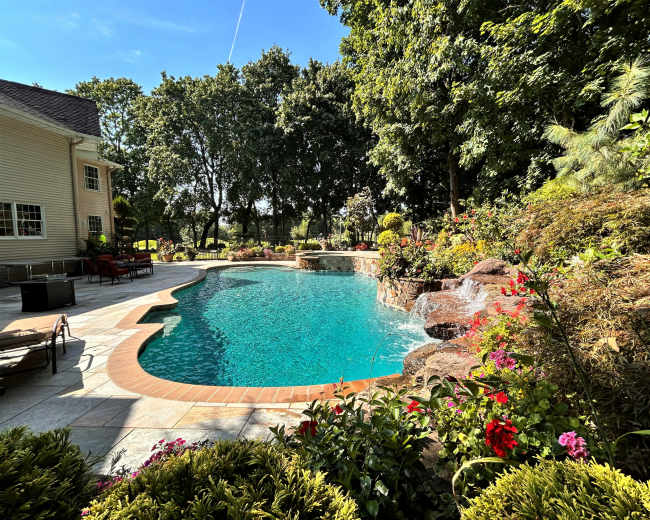 A backyard features a swimming pool surrounded by lush greenery and colorful flowers.