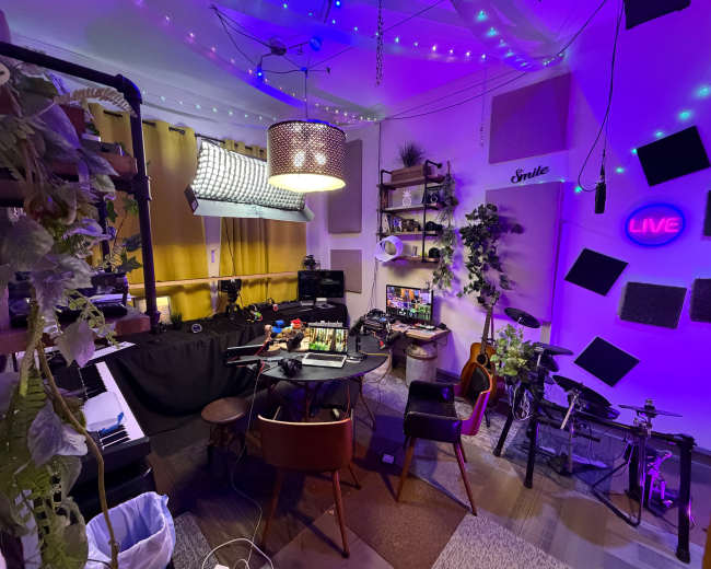 The image shows a vibrant, well-equipped creative studio featuring musical instruments, a table with equipment, and colorful lighting.