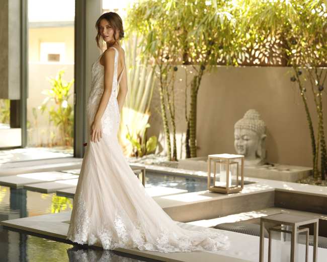 A bride stands elegantly in a lace wedding gown near a serene pool surrounded by greenery and decorative elements.