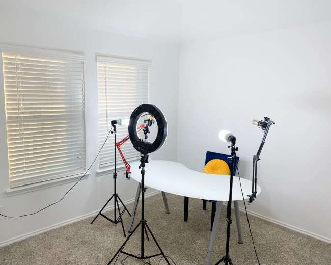 A bright, minimalistic room with a white table, a chair, and three lighting setups positioned around it.