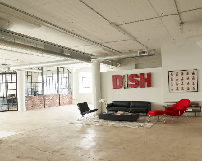 A spacious, modern office interior featuring a black sofa, a red chair, and industrial-style decor.