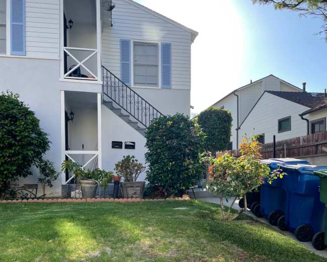 A two-story residential building with a staircase, potted plants, and several trash bins on the side.