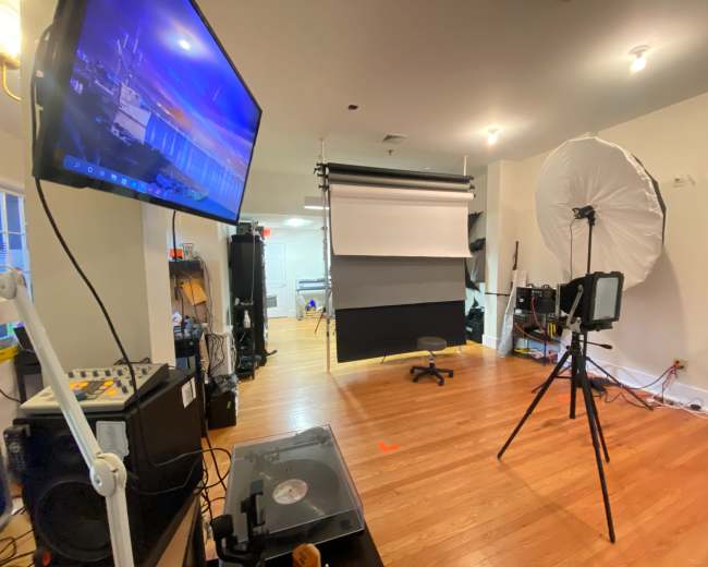 A photography studio is set up with a backdrop, lighting equipment, and a computer monitor displaying an image.