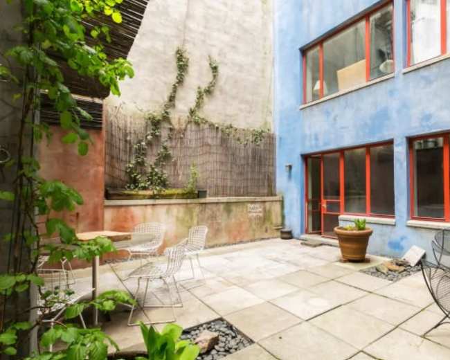 A small courtyard features stone paving, potted plants, and metal furniture surrounded by colorful walls.