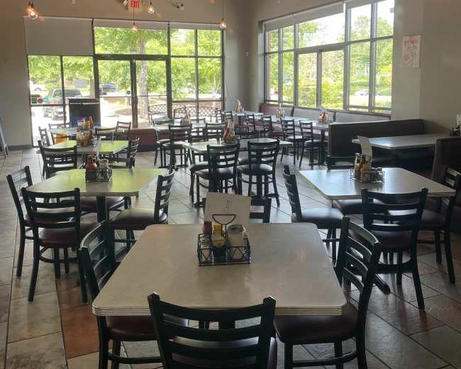 A spacious dining area of a restaurant featuring multiple tables and chairs arranged around a central section, with large windows letting in natural light.