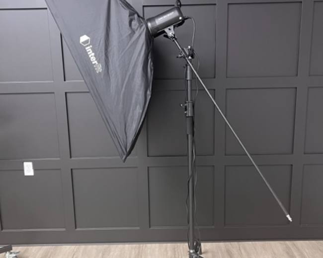 A light stand with a softbox attached, set against a black wall.