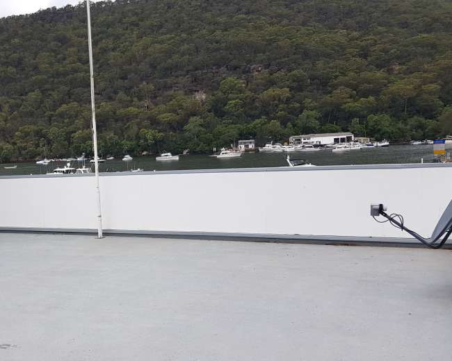 A rooftop terrace overlooks a body of water lined with boats and surrounded by green hills.
