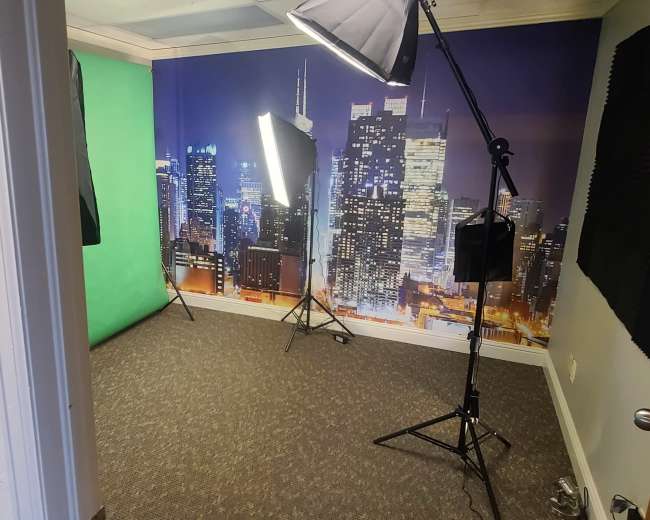 A studio setup featuring a green screen, softbox lights, and a city skyline backdrop.