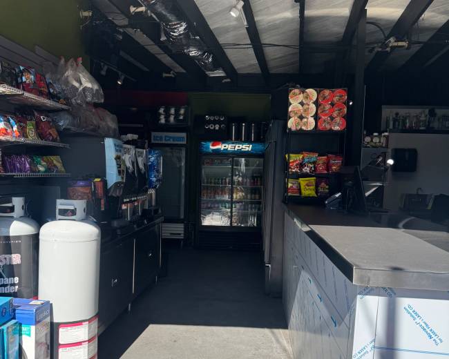 The image shows the interior of a convenience store with shelves stocked with snacks and beverages, including a Pepsi refrigerator in the background.