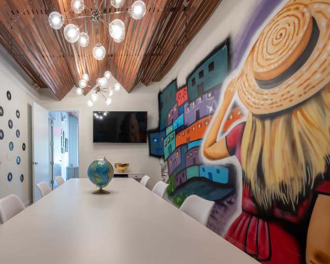 A modern conference room features a long white table, artistic wall murals, and decorative elements including vinyl records and a globe.