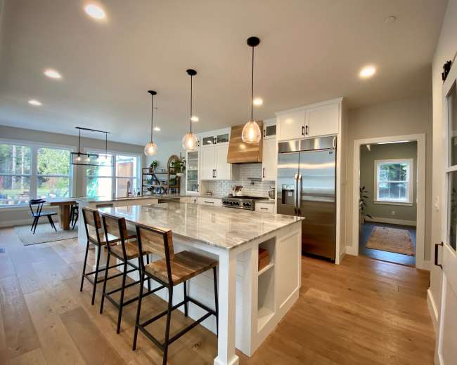 A modern kitchen with an island featuring bar stools, stainless steel appliances, and pendant lighting.