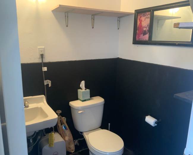 The image shows a small bathroom with a toilet, a sink, and a shelf mounted above the sink.