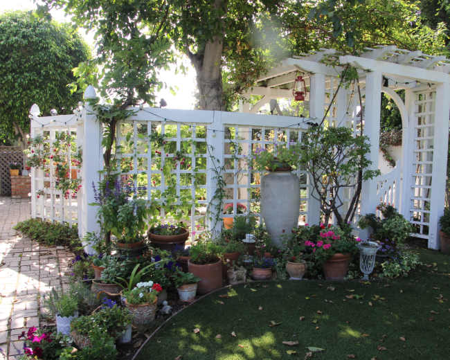A white lattice garden structure surrounded by various potted plants and flowers.