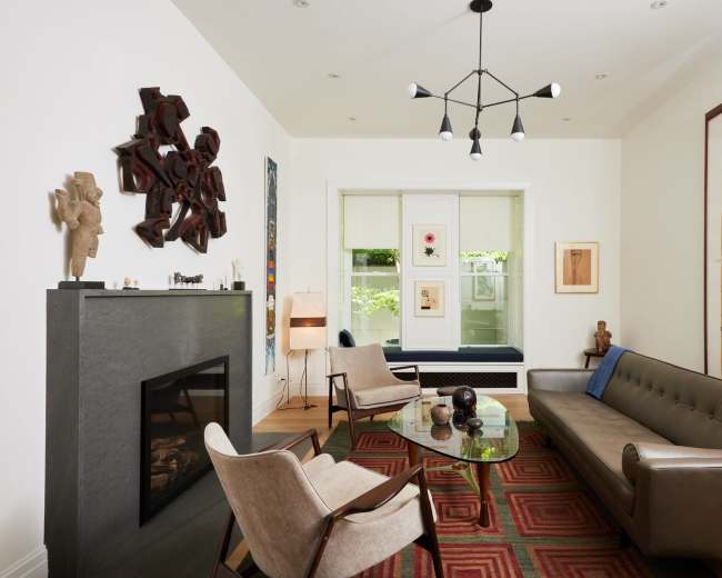 The image shows a modern living room with a beige sofa, a glass coffee table, and an art-adorned wall featuring various sculptures and framed artwork.
