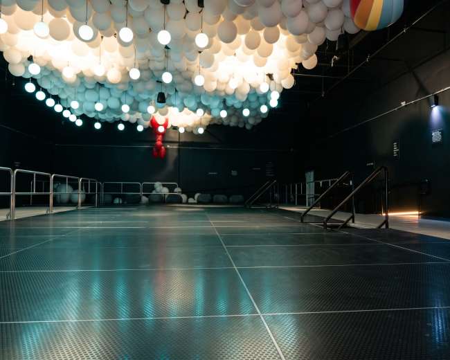 An empty industrial space features a smooth, reflective floor and a ceiling adorned with colorful, suspended lights.