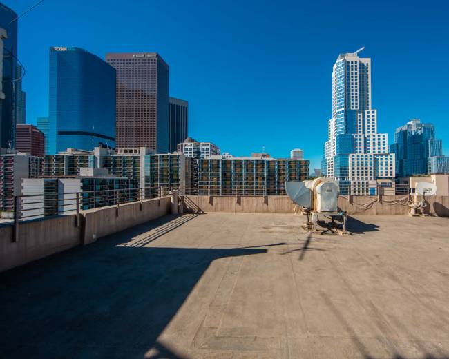 The image shows a rooftop with satellite dishes, overlooking a skyline of tall buildings against a clear blue sky.