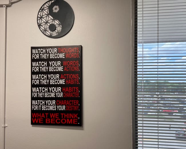 The image shows a wall with a motivational poster featuring the phrases "Watch your thoughts," "Watch your words," "Watch your actions," "Watch your habits," and "Watch your character," alongside a circular yin-yang symbol.