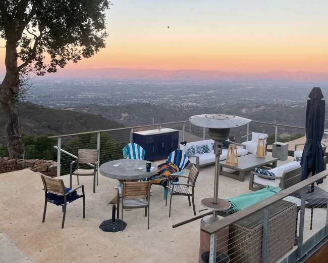 A spacious outdoor patio area with seating and tables, overlooking a valley during sunset.